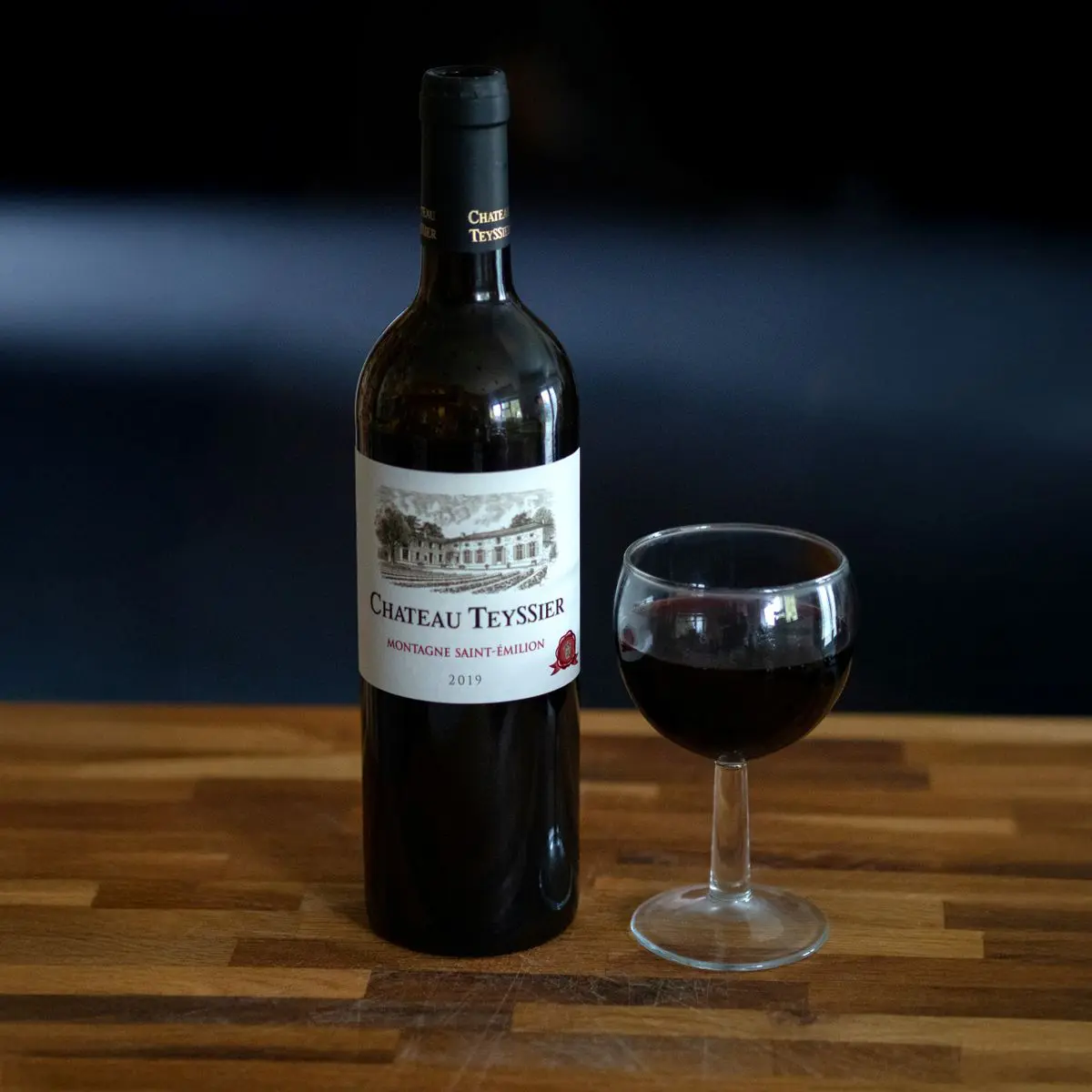 Bouteille de vin rouge et verre rempli posés sur une table en bois, idée cadeau vin