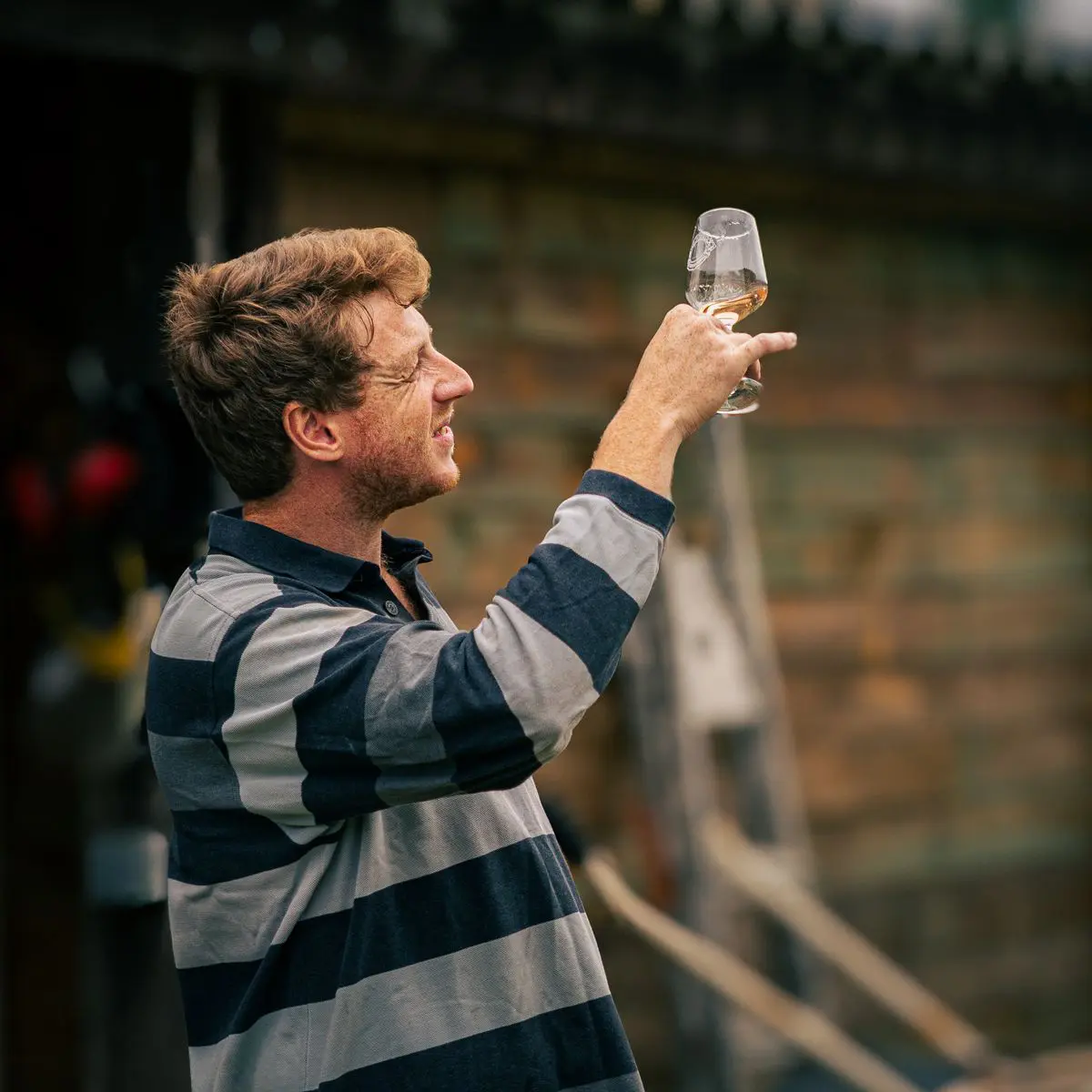 Un vigneron indépendant de Nouvelle-Aquitaine inspecte un verre de vin en extérieur, gage de qualité