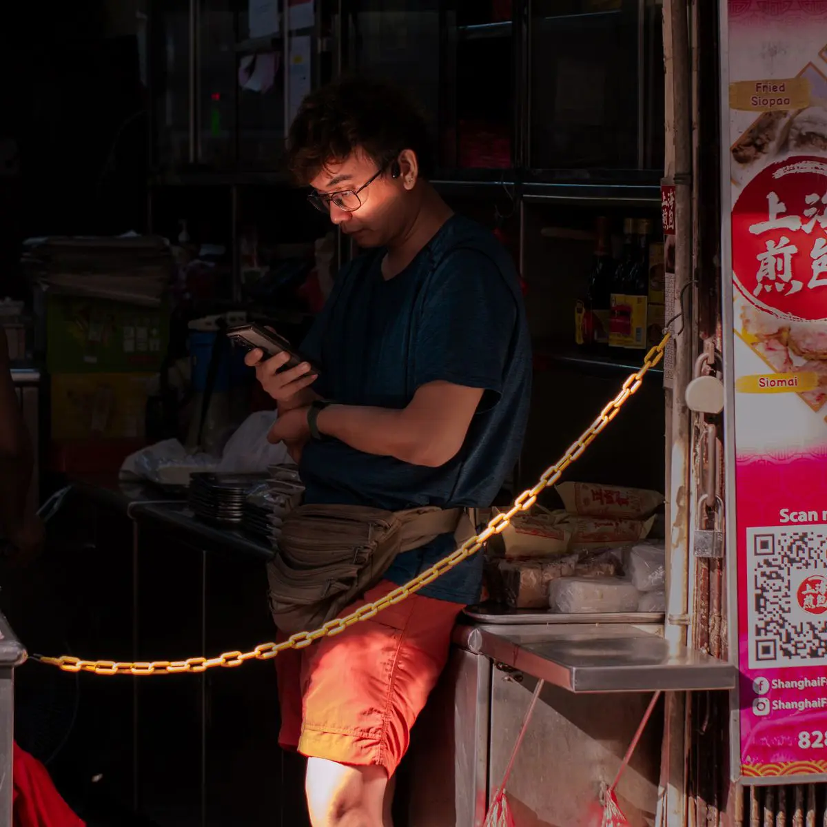 Un homme utilise son smartphone sur un stand de marché, éclairé par la lumière du soleil